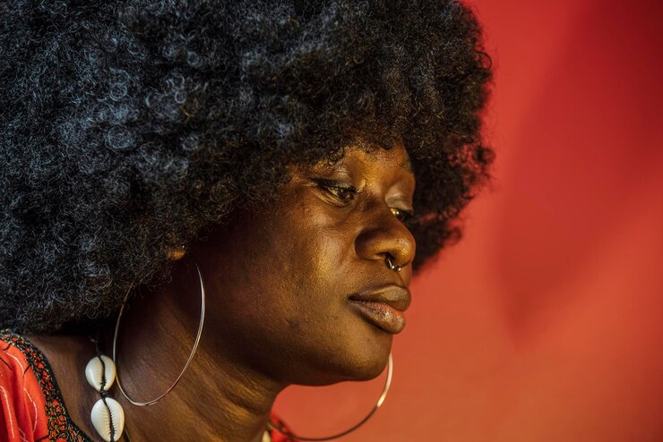 Photo face de femme africaine à l'intérieur avec une lumière orange et des cheveux traditionnels africains