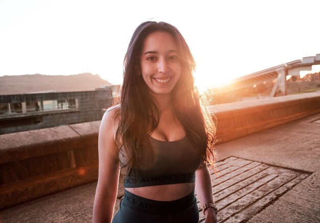 face frontale Jeune femme athlète africaine souriante à la caméra se reposant pendant le coucher du soleil. Formation à l'espace urbain au concept de ville, béton. Mode de vie actif sur les jeunes. S'entraîner avec des amis est amusant