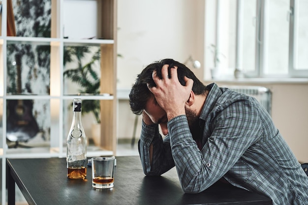 La façon la plus courante pour les gens d'abandonner leur pouvoir est de penser qu'ils n'en ont pas. Homme ivre avec verre et bouteille de whisky assis à table dans la cuisine. Boire seul. Concept d'alcoolisme masculin