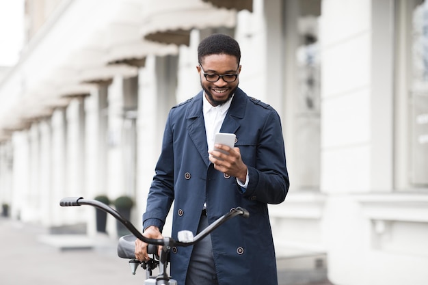 Façon de travailler Jeune homme envoyant des SMS au téléphone debout avec un vélo dans l'espace libre de la rue de la ville