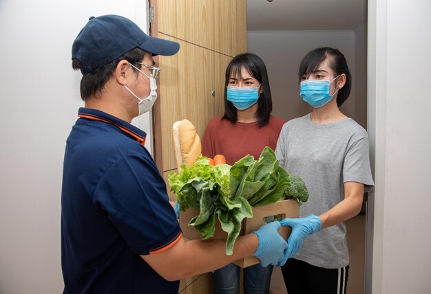 Le facteur porte un masque pour couvrir le transport de légumes à une femme devant la livraison de nourriture à domicile