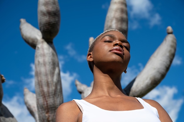 Faible angle de femme afro-américaine détendue debout avec les yeux fermés contre le dragonnier