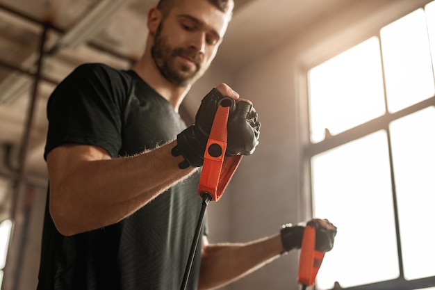 Faible angle d'homme barbu musclé confiant dans des gants d'entraînement faisant de l'exercice avec une bande de résistance élastique pendant l'entraînement fonctionnel en salle de sport