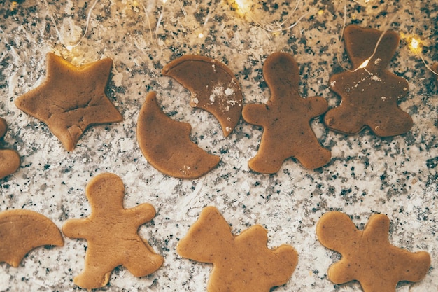 Photo faire des biscuits de noël figurés biscuits au pain d'épice sur la table de la cuisine avec des lumières de noël