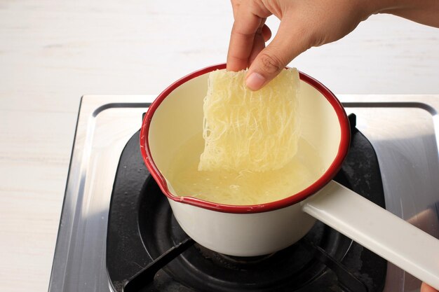 Faire bouillir du verre ou des vermicelles de nouilles de riz sur une casserole en émail au-dessus de la cuisinière Ajouter des nouilles à la casserole Activité de cuisine maison