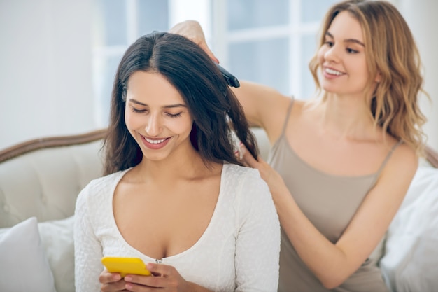 Faire des cheveux. Jolie fille blonde faisant des cheveux à sa petite amie souriante