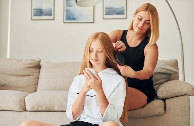 Faire la coiffure Une adolescente avec sa mère est à la maison pendant la journée