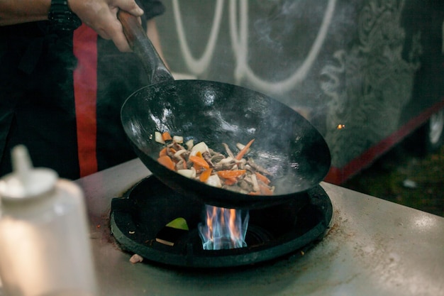 faire cuire des frites de légumes dans une poêle à wok en feu Chef cuisinant à la flamme dans une poêle à frire