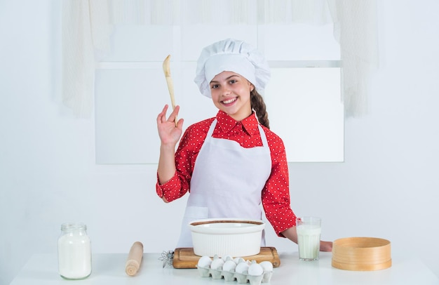 Faire du gâteau par recette le temps de manger enfant heureux cuisiner dans la cuisine cuire des biscuits dans la cuisine enfant boulanger professionnel et qualifié en uniforme de chef et chapeau adolescente préparant la pâte