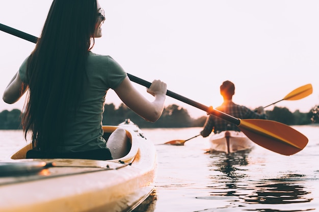 Faire du kayak en couple. Vue arrière du beau jeune couple kayak sur la rivière avec coucher de soleil en arrière-plan