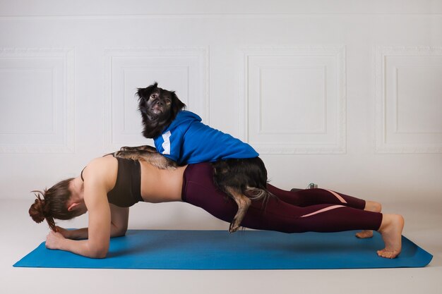 Faire du sport avec un chien. Jolie fille travaillant sur le tapis de fitness bleu avec son chien. Femme athlétique faisant de l'exercice. Force et motivation, sport et mode de vie sain. Remise en forme féminine.