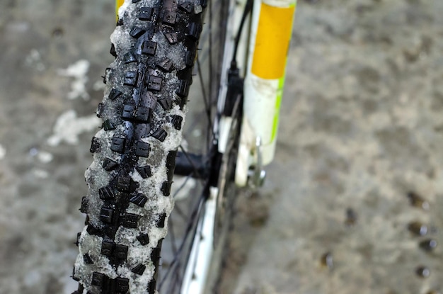 Faire du vélo en hiver Pneu de vélo recouvert de neige Vélo dans l'atelier pour réparation Gros plan sur la roue avant et la neige Grandes pointes sur un pneu épais