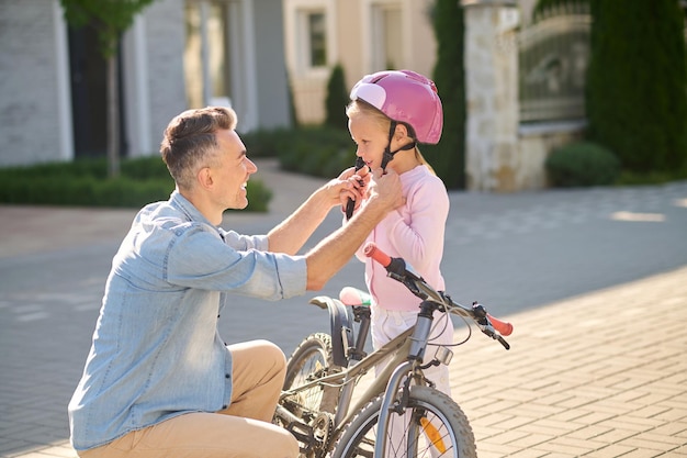 Faire du vélo. Un homme met un casque de protection sur la tête de sa fille avant de faire du vélo