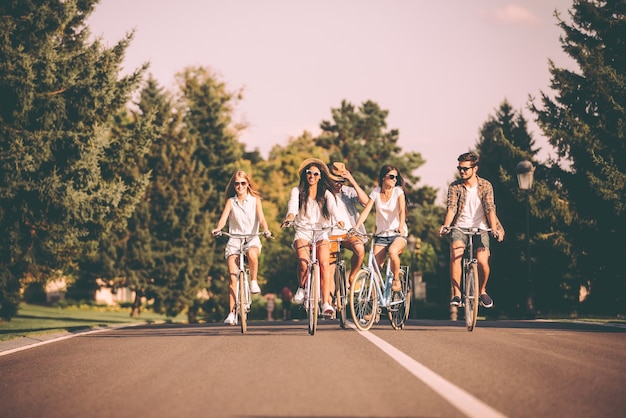 Faire du vélo avec plaisir. Groupe de jeunes faisant du vélo le long d'une route et ayant l'air heureux