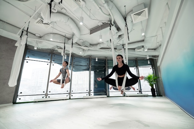 Faire du yoga volant. Les femmes et les hommes portant des vêtements de sport se sentent incroyables en faisant du yoga volant