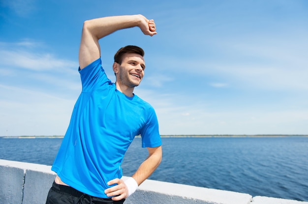 Faire de l'exercice à l'extérieur. Beau jeune homme faisant des exercices d'étirement en se tenant debout à l'extérieur