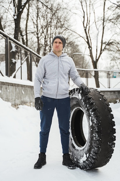 Faire de l'exercice avec un gros pneu Sportif fort pendant son entraînement croisé pendant une journée d'hiver enneigée et froide