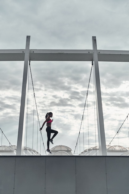 Faire de l'exercice en plein air. Toute la longueur d'une jeune femme moderne en vêtements de sport sautant tout en faisant de l'exercice à l'extérieur