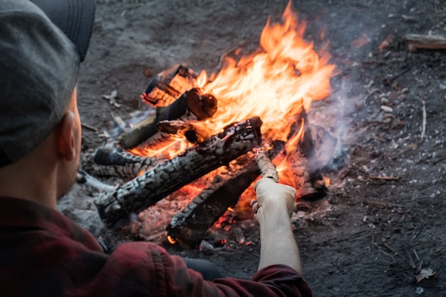 Faire un feu de camp dans une forêt. Un homme en tenue décontractée met des morceaux de bois dans un feu brûlant.