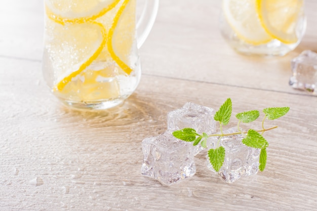 Faire fondre des glaçons, des feuilles de menthe fraîche et de l'eau citronnée dans un verre sur une table en bois