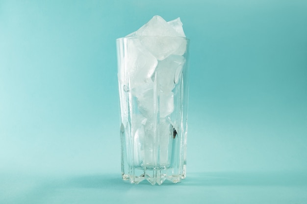 Faire fondre des morceaux de glace dans un verre sur une surface bleue.
