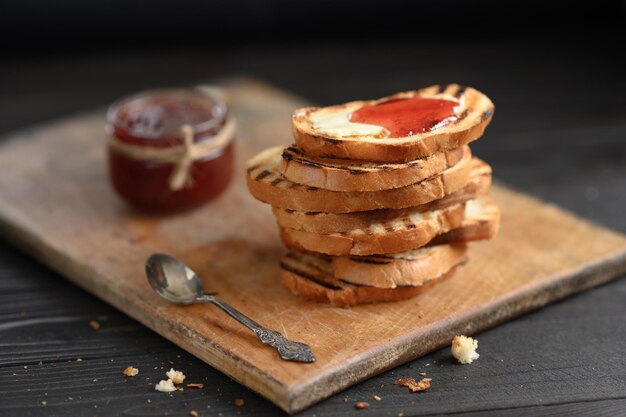 Faire griller du pain avec de la confiture de fraises maison et sur une table rustique avec du beurre pour le petit-déjeuner ou le brunch