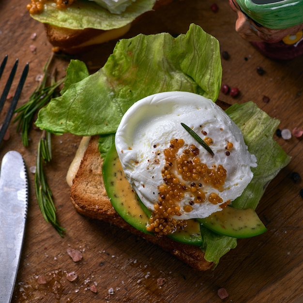 Faire griller du pain avec des tranches d'avocat, des œufs en sachet et des légumes verts sur une planche à découper en bois.