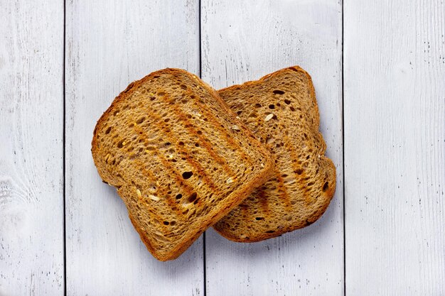 Faire griller des tranches de pain de blé entier sur fond blanc en bois