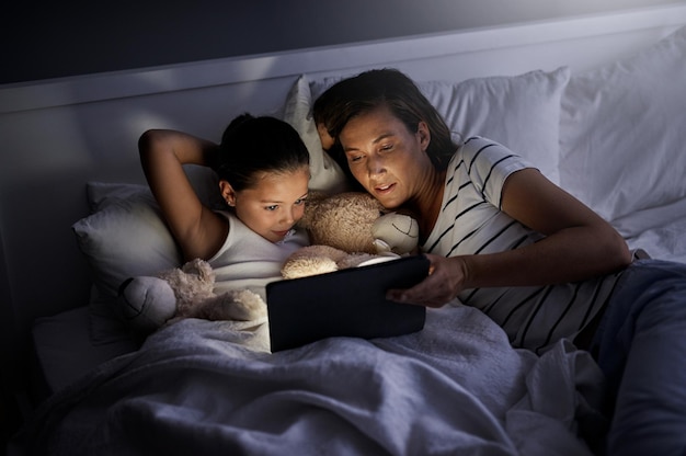 Faire l'heure du conte un peu différemment Photo d'une mère et de sa petite fille utilisant une tablette numérique ensemble au lit la nuit