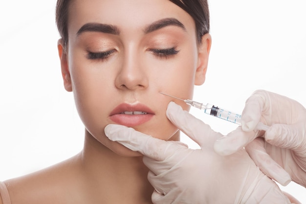 Faire une injection de botox Belle jeune femme torse nu gardant les yeux fermés pendant que les médecins font une injection dans le visage