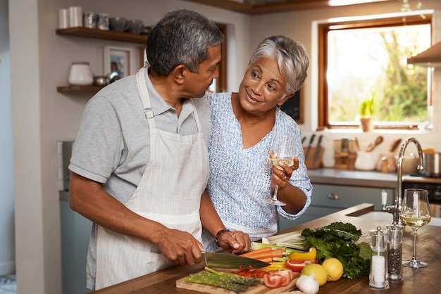 Faire de leur retraite une délicieuse photo d'un couple d'âge mûr heureux buvant du vin tout en cuisinant un repas ensemble à la maison