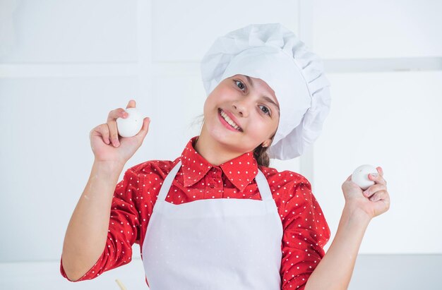 Faire de la nourriture spéciale heureuse adolescente tenant des oeufs enfant porter l'uniforme de chef dans la boulangerie