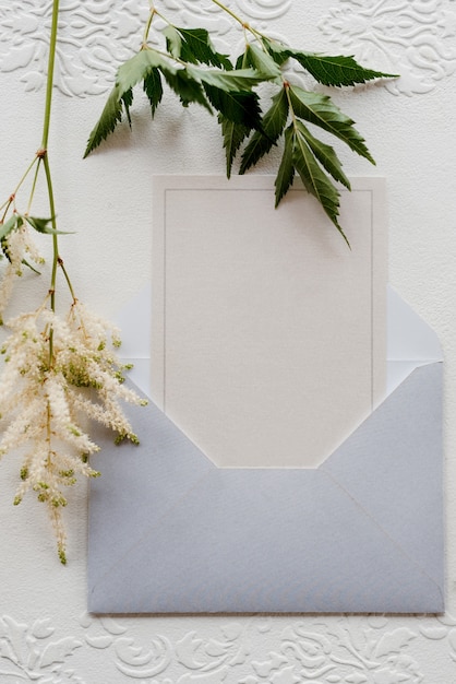 Faire-part de mariage dans une enveloppe grise sur une table avec des brins verts