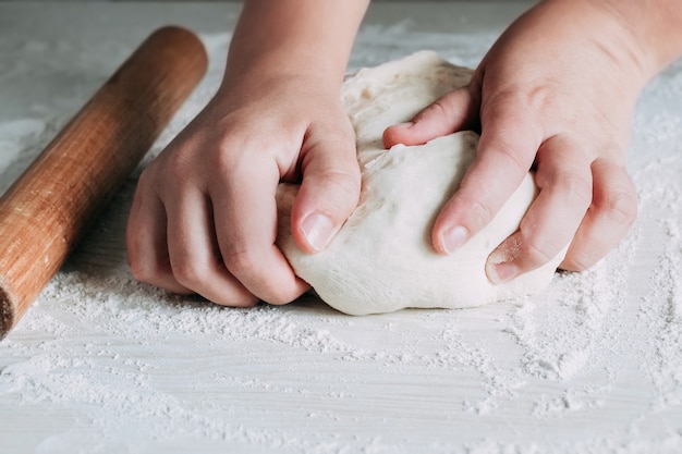 Faire de la pâte par des mains féminines sur fond de table en bois blanc