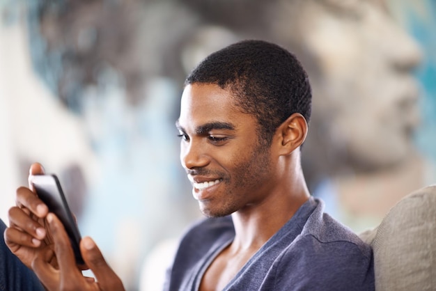 Faire des plans avec un ami Photo recadrée d'un beau jeune homme utilisant son téléphone portable tout en se relaxant à la maison