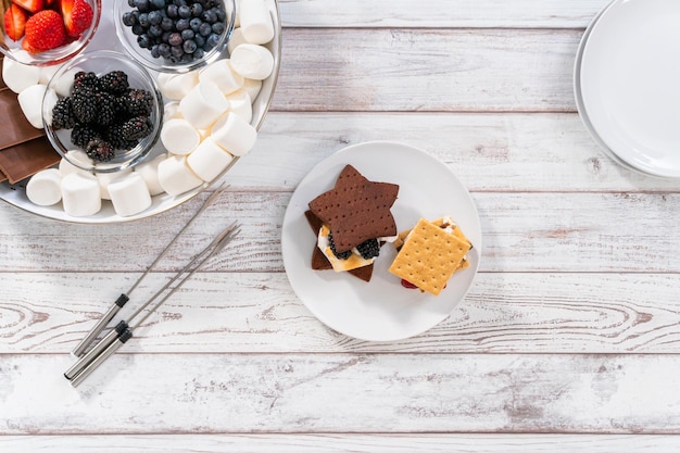 Faire des s'mores sur un biscuit graham au chocolat en forme d'étoile fait maison avec de la guimauve grillée et des fruits.