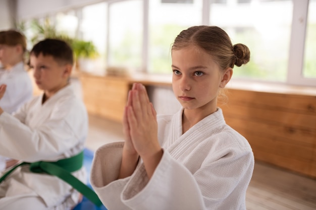 Faire signe Namaste. Jolie fille aux cheveux blonds apprenant l'aïkido en faisant un signe de Namaste