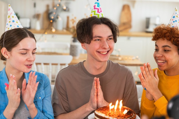 Faire un vœu homme portant une casquette de fête soufflant des bougies allumées sur un gâteau d'anniversaire joyeux anniversaire