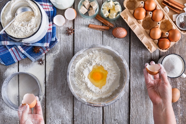 Faire la vue de dessus de la pâte. Les frais généraux des mains du boulanger casser l'oeuf sur la farine. Ingrédients de cuisson pour pâtisserie sur bois rustique, cours de cuisine ou concept de recette.