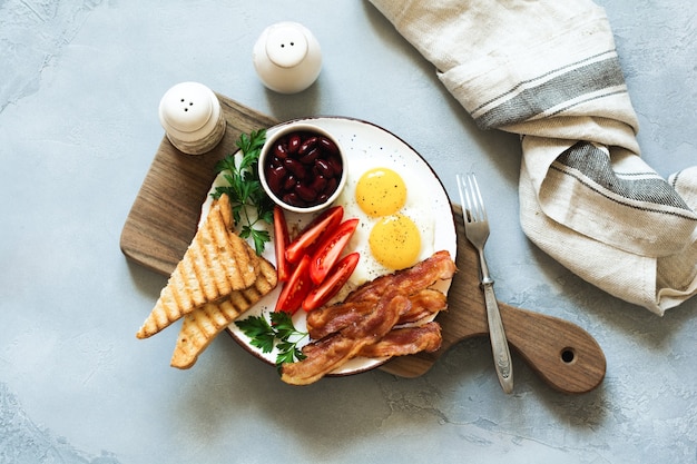 Faites frire le petit-déjeuner anglais traditionnel avec des œufs au plat, des saucisses, du bacon, du boudin noir, des haricots, des toasts et du thé sur fond de béton gris. Vue de dessus