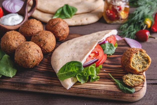 Falafel, légumes frais, sauce et pain pita sur table en bois