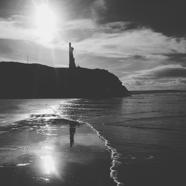 Photo une falaise en silhouette sur la plage contre un ciel nuageux au coucher du soleil