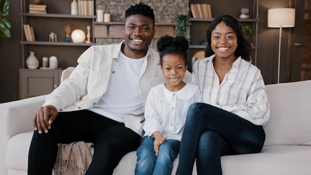 Une famille africaine s'assoit sur un canapé confortable dans le salon Parents biraciaux et enfant souriant