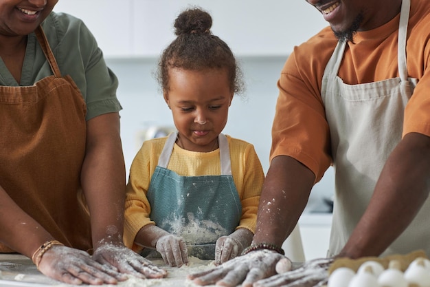 Famille afro-américaine cuisinant avec un enfant dans la cuisine, ils font de la pâte à table