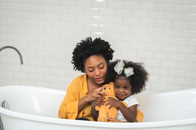 Famille afro-américaine, mère heureuse et petite fille s'amusant et jouant ensemble dans la salle de bain, fond de mur blanc