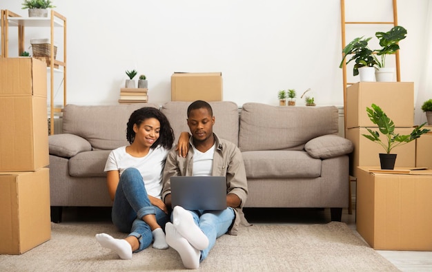 Famille afro-américaine vérifiant des idées d'intérieur pour un nouvel appartement, à l'aide d'un ordinateur portable