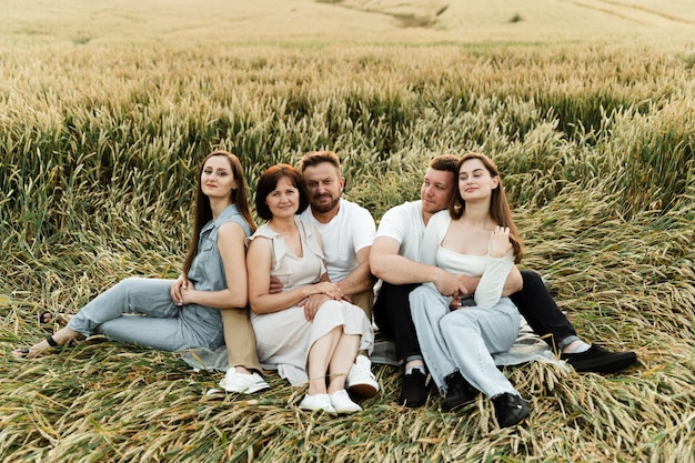 Une famille d'agriculteurs est assise dans un champ de blé au coucher du soleil et se réjouit, récolte biologique, le blé écologique est cultivé par une famille, une famille de cinq personnes se repose dans un champ