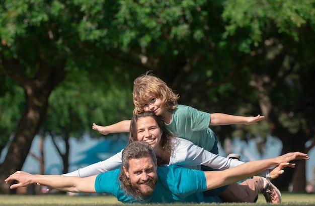 Photo famille allongée sur l'herbe dans le parc parents donnant enfant piggybacks à la campagne concept de mouche petit garçon