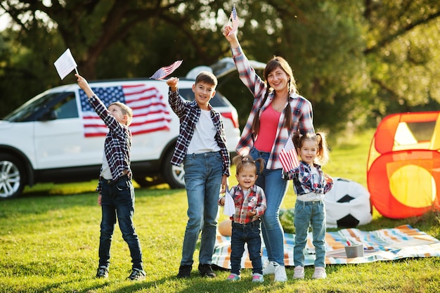 Une famille américaine passe du temps ensemble avec des drapeaux américains contre une grosse voiture suv en plein air