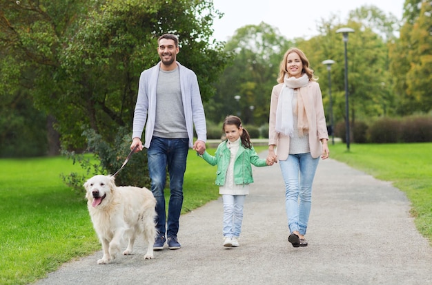 famille, animal de compagnie, animal domestique et concept de personnes - famille heureuse avec chien labrador retriever marchant dans le parc d'été